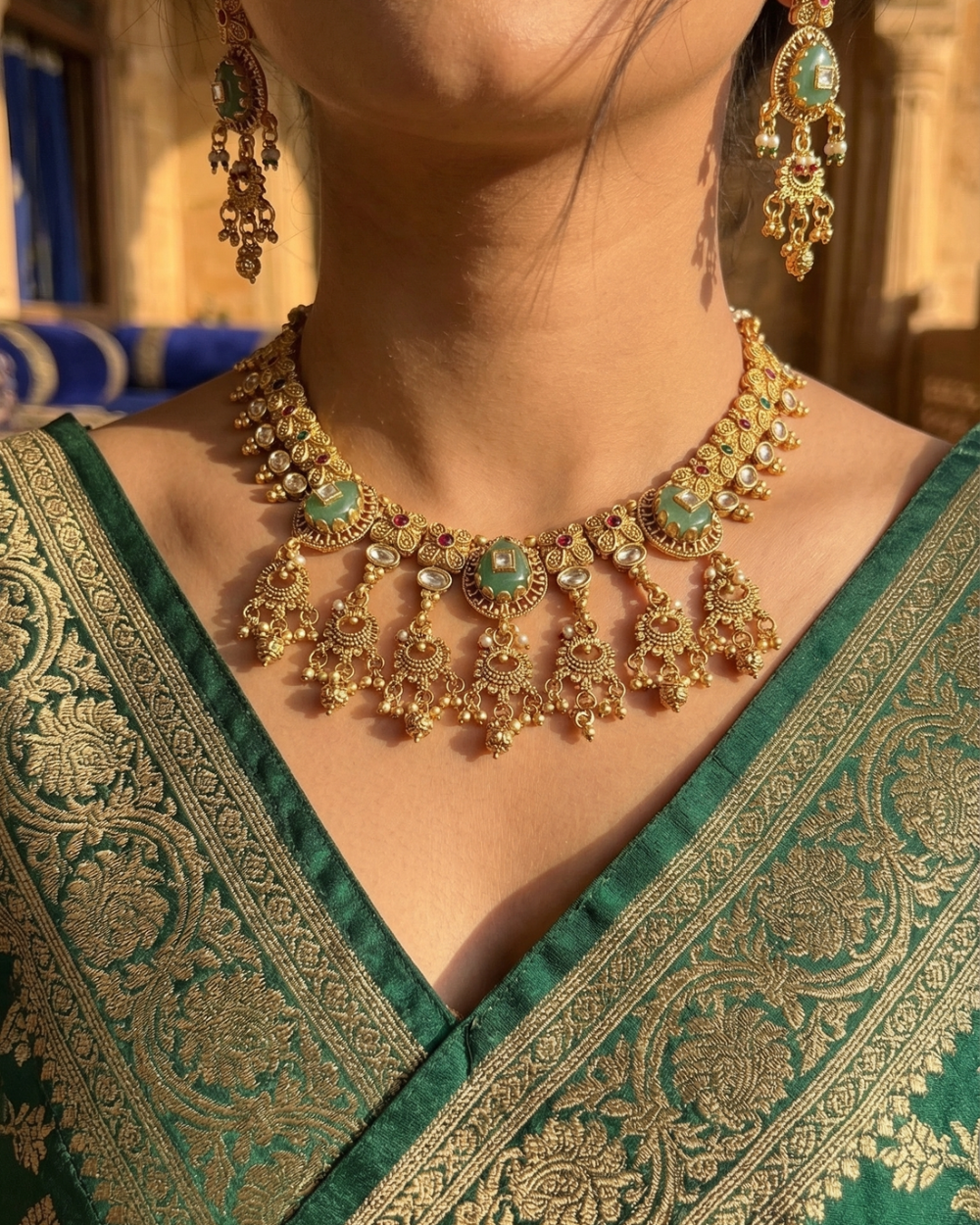Gold necklace and earrings on a person wearing a green and gold saree.